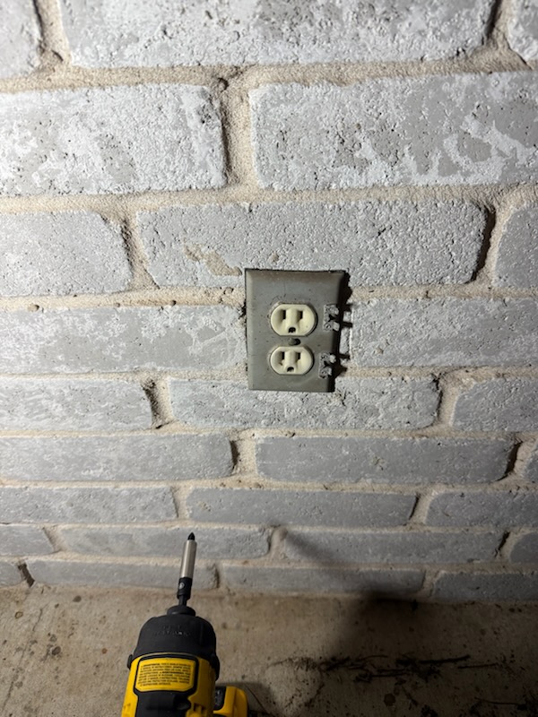Older exterior duplex outlet mounted on a brick wall before replacement
