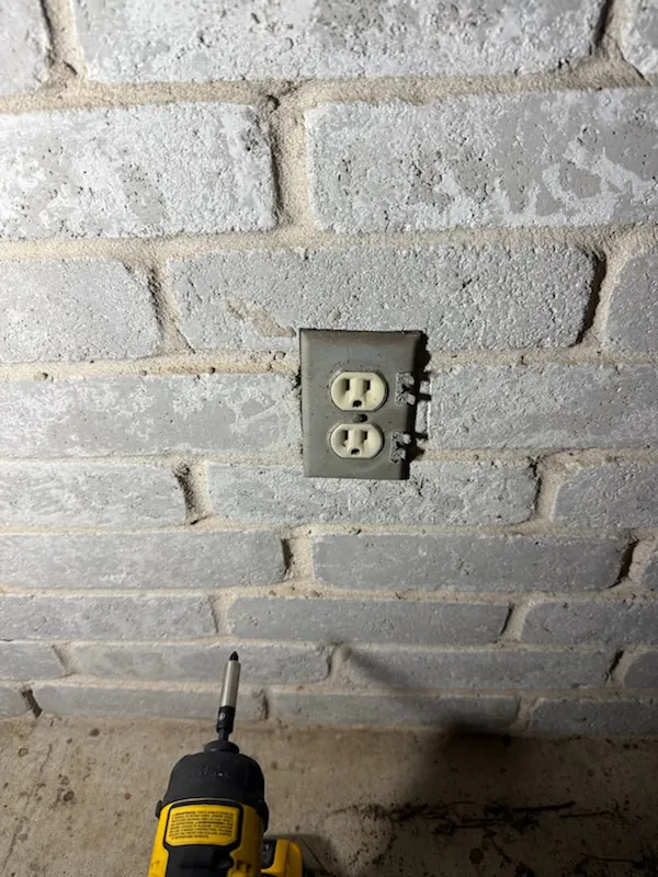 Older exterior duplex outlet mounted on a brick wall before replacement